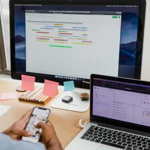 Businessman multitasks with smartphone, laptop, and monitor in office setting.