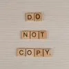 Close-up of wooden tiles spelling 'Do Not Copy' on a textured surface.